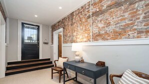 A room with a brick wall, a desk with drawers, a chair, and a lamp.
