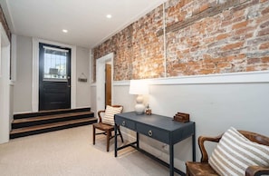 A room with a brick wall, a desk with drawers, a chair, and a lamp.