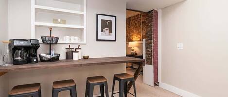 A kitchen with a bar area, stools, a coffee maker, and a framed picture on the wall.