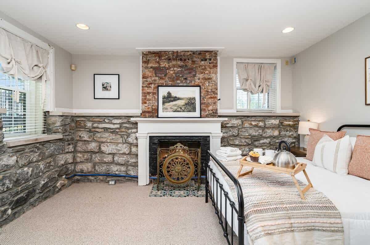 A bedroom with a stone fireplace, a bed with a patterned bedspread, and a window with curtains.