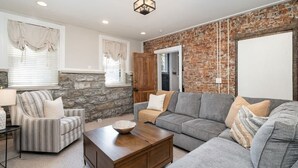 A living room with a stone accent wall, a grey sofa, a striped armchair, and a wooden coffee table.