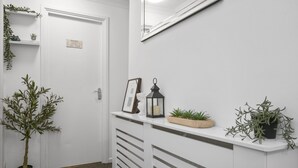 A hallway with a white door, a mirror, a shelf with plants, and a framed picture.