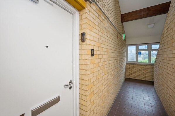 A hallway with a white door, yellow brick walls, and a window at the end.