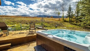 A hot tub on a wooden deck with outdoor furniture, surrounded by a natural landscape with trees and mountains in the background. - Aspen - Casa Connable (Aspen)