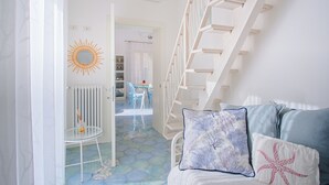 Un escalier menant à un deuxième étage, un radiateur blanc, un miroir rond, une table avec des chaises et un sol à motifs.