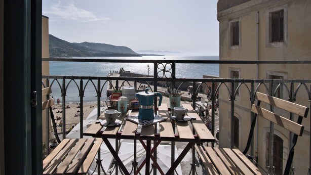 Un balcon avec vue sur la mer, des meubles en bois et une table sur laquelle se trouvent divers objets.