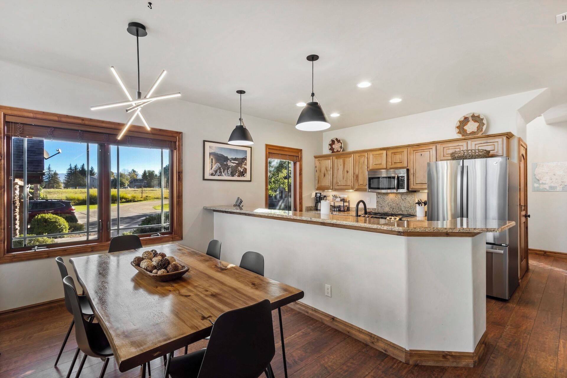 Une cuisine moderne dotée d’un îlot central, de meubles en bois, d’appareils électroménagers en acier inoxydable et de luminaires suspendus.