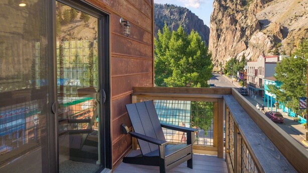 A balcony with a wooden railing, a black chair, and a view of a town with buildings and a mountain in the background.