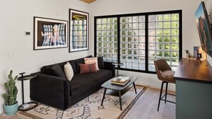 A modern living room with a black sofa, a coffee table, a cactus plant, and a large window with a view of greenery.