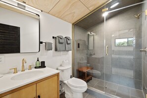 A modern bathroom with a white sink, gold faucets, a toilet, and a glass-enclosed shower.