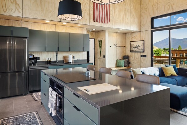 A modern kitchen with a central island, stainless steel appliances, and a large window offering a mountain view.