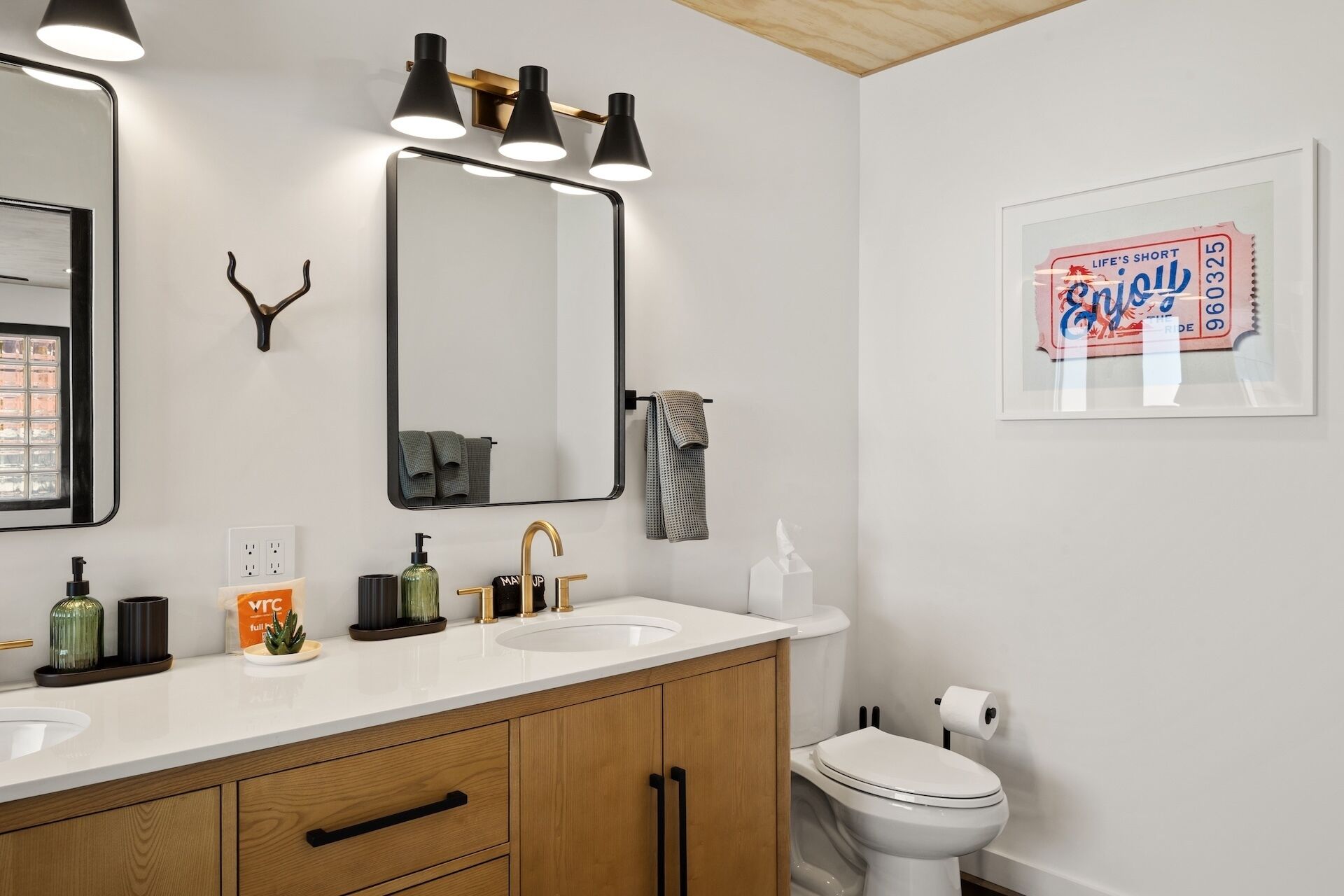 A bathroom with a white sink, a mirror, and a toilet. There is a framed sign on the wall and a towel rack.