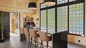 A modern kitchen with a bar area, wooden cabinetry, and large windows with a view.