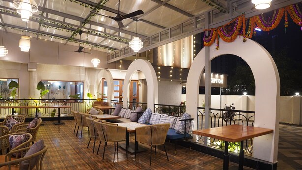 A restaurant with wooden flooring, wicker furniture, and a view of the city at night. - Hotel Status Inn (Ambernath)