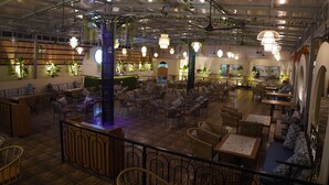 A spacious indoor dining area with multiple seating arrangements, including tables and chairs, and a central decorative pillar. - Hotel Status Inn (Ambernath)