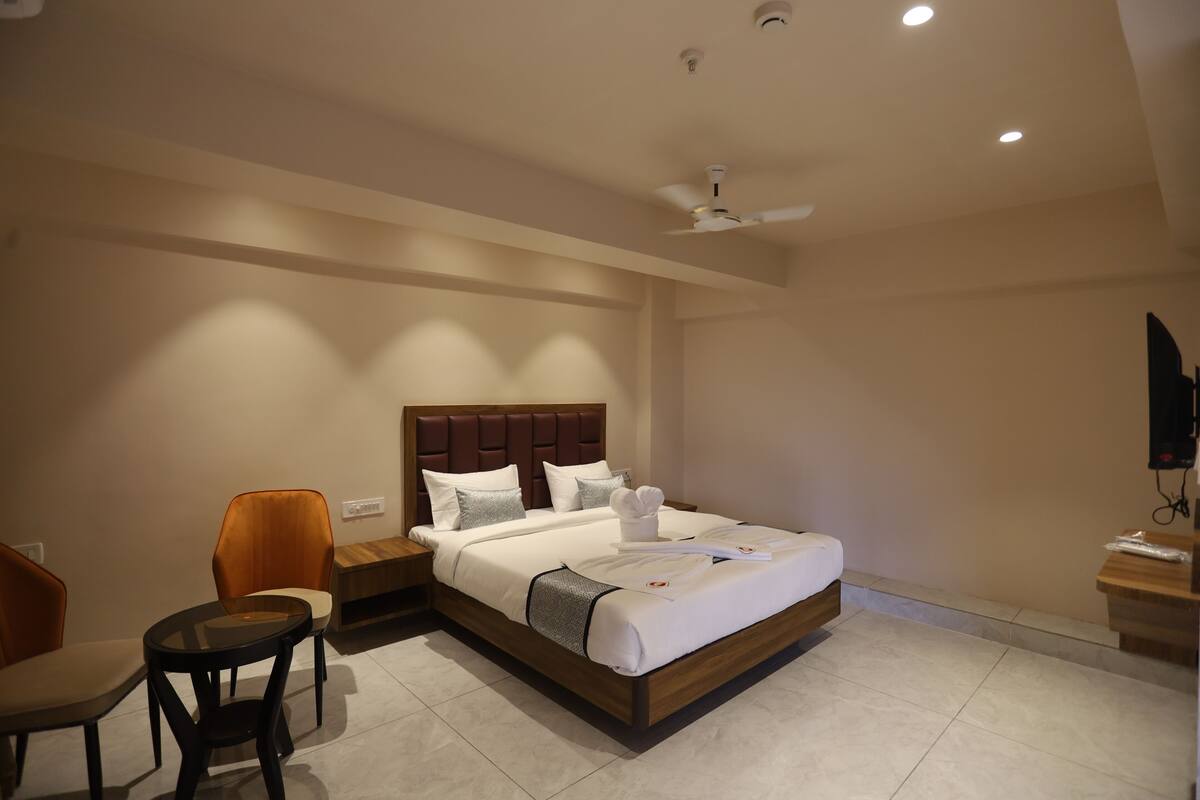 A hotel room with a large bed, a bedside table, a chair, a desk, and a ceiling fan.