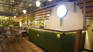A reception area with a green wall, wooden floor, wicker furniture, and hanging plants. - Hotel Status Inn (Ambernath)