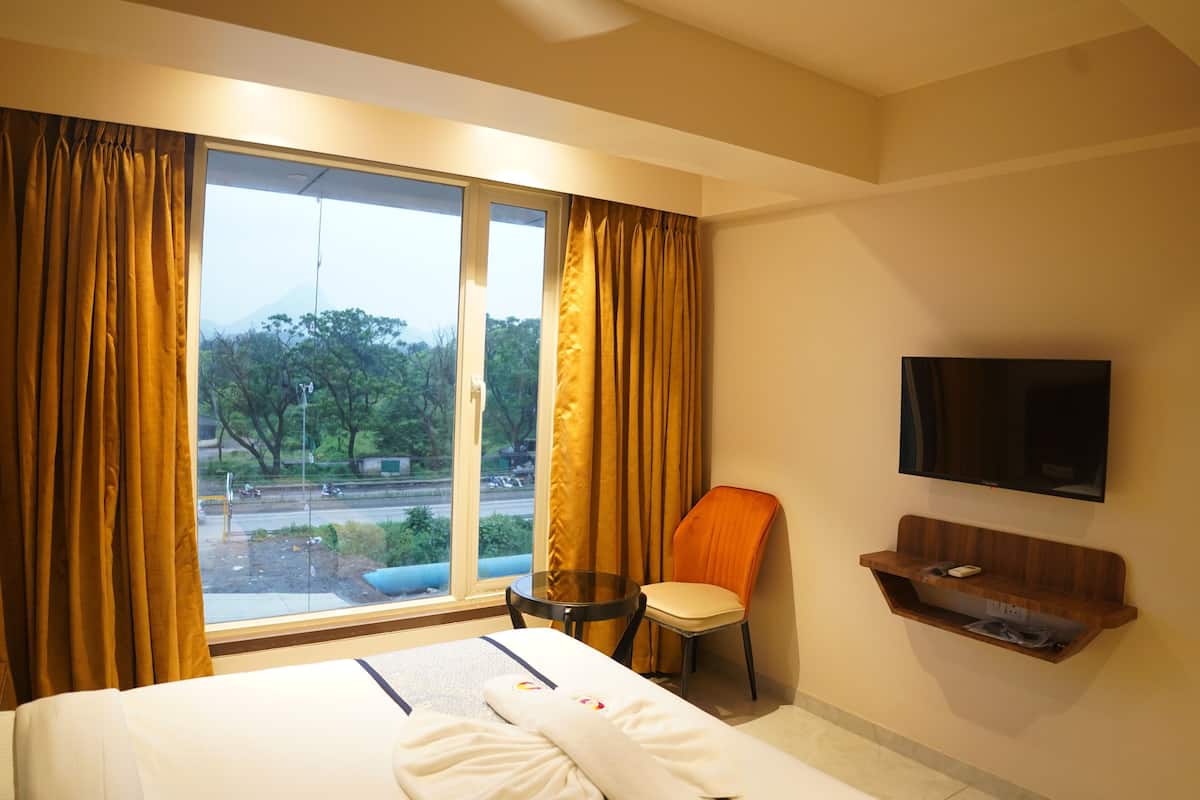 A hotel room with a bed, a chair, a small table, a TV, and a window with curtains.