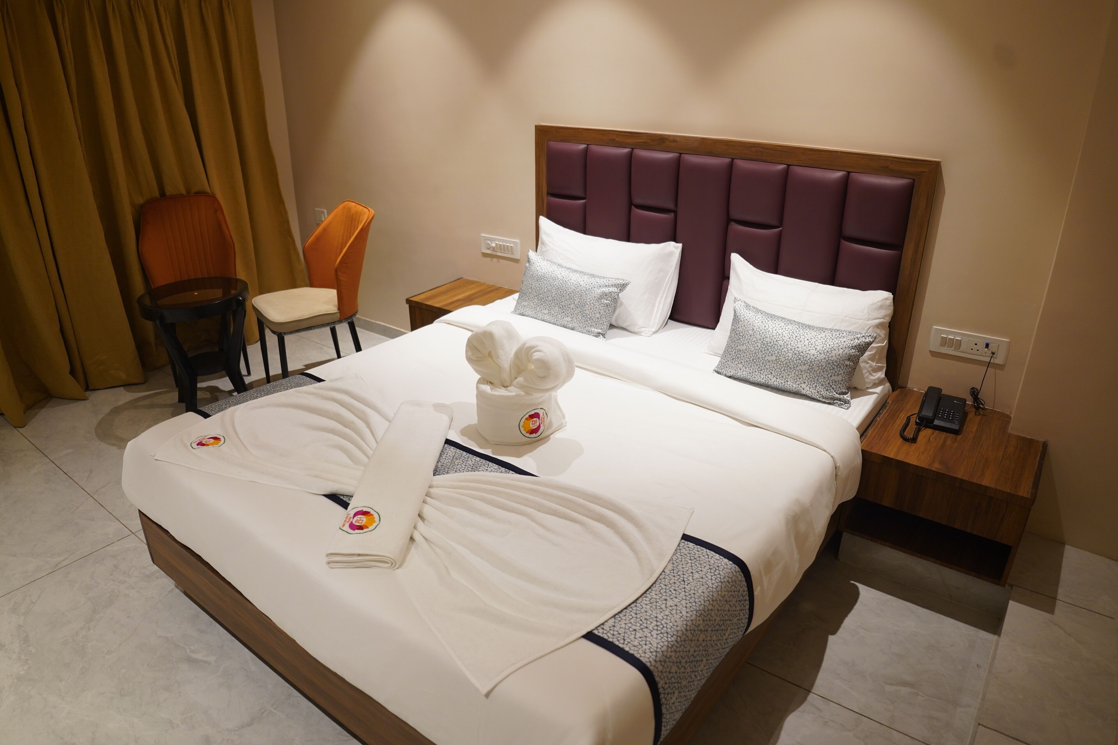 Una habitación de hotel con una cama grande, una mesita de noche de madera, una silla y una cortina.