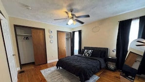 Un dormitorio con cama, ventilador de techo, piso de madera y una puerta.