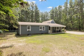 A single-story house with a covered porch, a fenced yard, and a forested backdrop. - Lake Escape Family & Pet Friendly with Dock Access (Freedom)