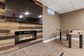 A room with a fireplace, a foosball table, and a television mounted on the wall. - Lake Escape Family & Pet Friendly with Dock Access (Freedom)
