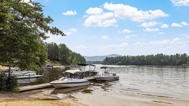 Un moll al costat d'un llac amb barques, una platja de sorra i una riba boscosa.