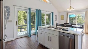 A kitchen with a large island, white cabinets, and a dishwasher. There is a sliding glass door leading to a balcony. - Nanas Nest - Lakefront Studio on Lovell Lake (Wakefield)