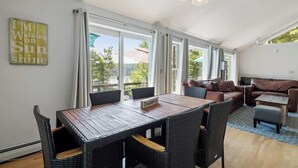 A spacious living area with a dining table, wicker furniture, and a view through large windows. - Nanas Nest - Lakefront Studio on Lovell Lake (Wakefield)