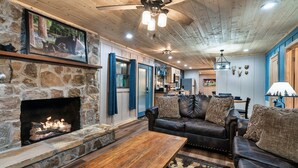 A cozy living room with a stone fireplace, leather sofas, and a ceiling fan.