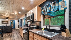 A modern kitchen with wooden cabinets, a stainless steel sink, and a large window overlooking a forest.