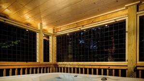 A hot tub in a wooden cabin with a view of the night sky through large windows.