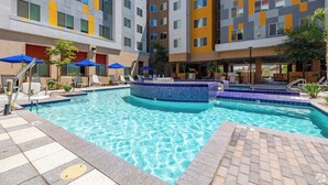 A hotel pool area with multiple levels of balconies, lounge chairs, and umbrellas.