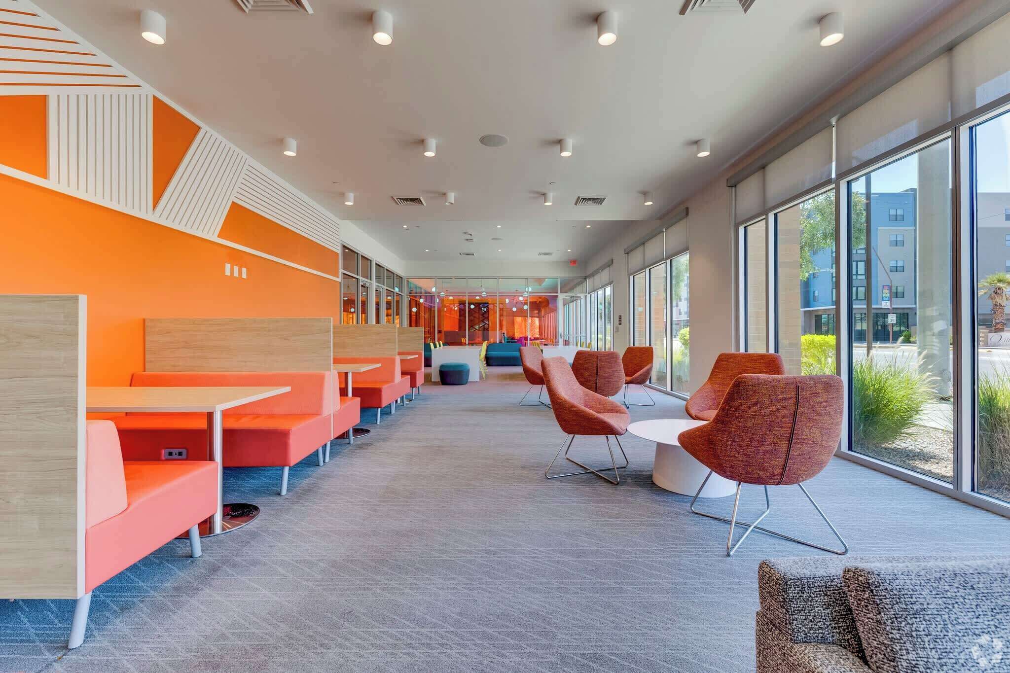 Um espaço interno moderno com assentos laranja, janelas grandes e vista para o exterior.