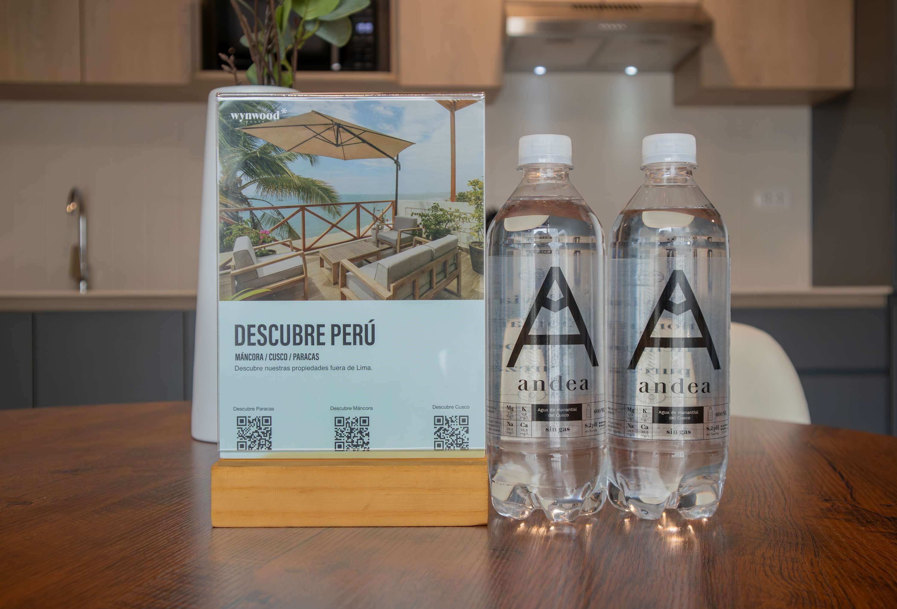 Un depliant dal titolo 'DESCUBRE PERÚ' con codici QR, due bottiglie d'acqua 'andea' e un tavolo di legno in una cucina moderna.