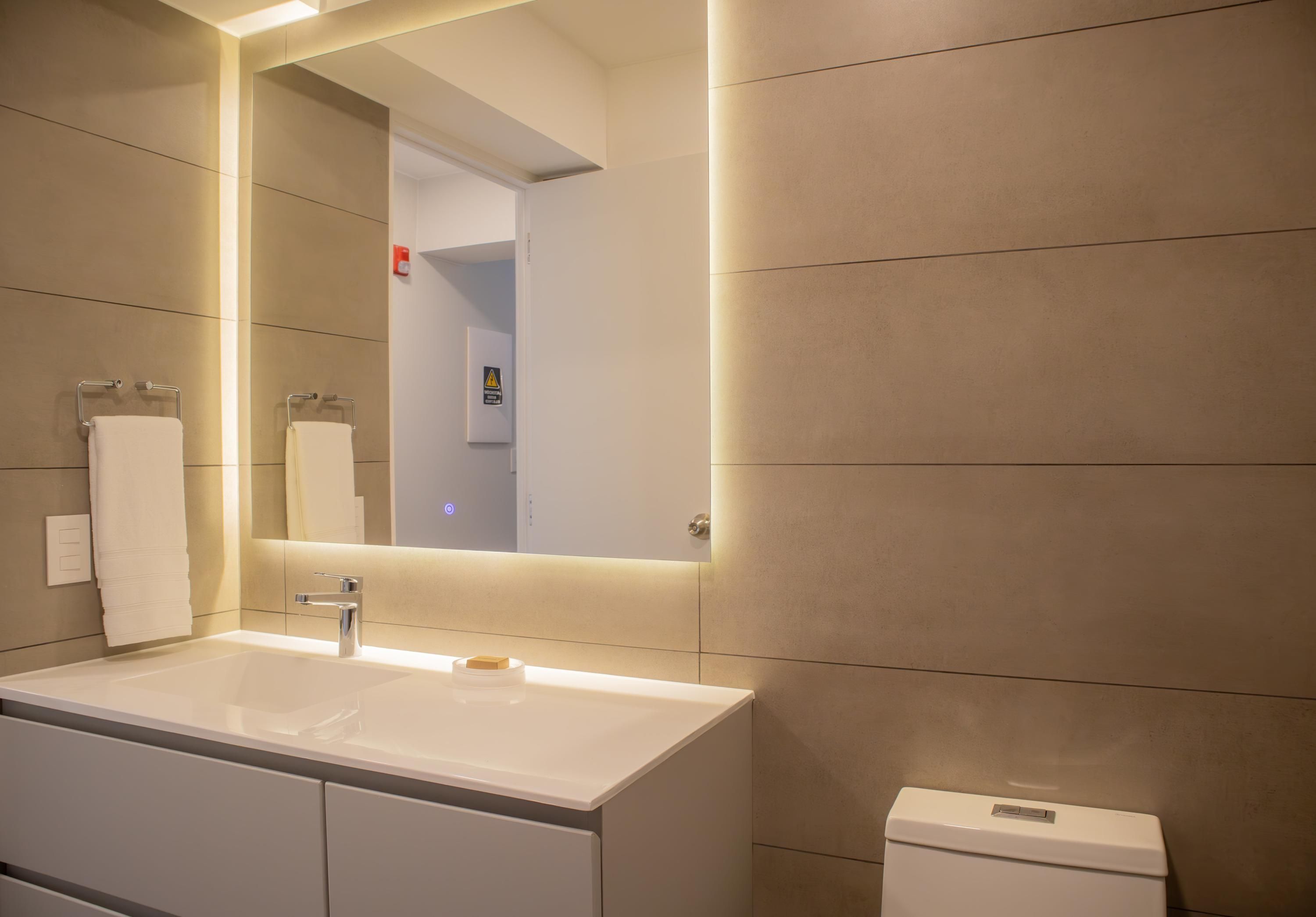 A modern bathroom with a large mirror, a white sink, and a toilet.