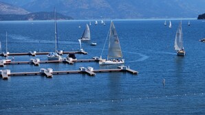 A marina with multiple sailboats docked at wooden piers, surrounded by calm water and distant mountains. - Fresh Design, King & Queen - Seasons at Sandpoint (Sandpoint)
