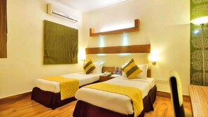 A hotel room with two beds, a wooden floor, a green wall, and a ceiling-mounted air conditioner. - Sk Premium Park GGN (Gurugram)