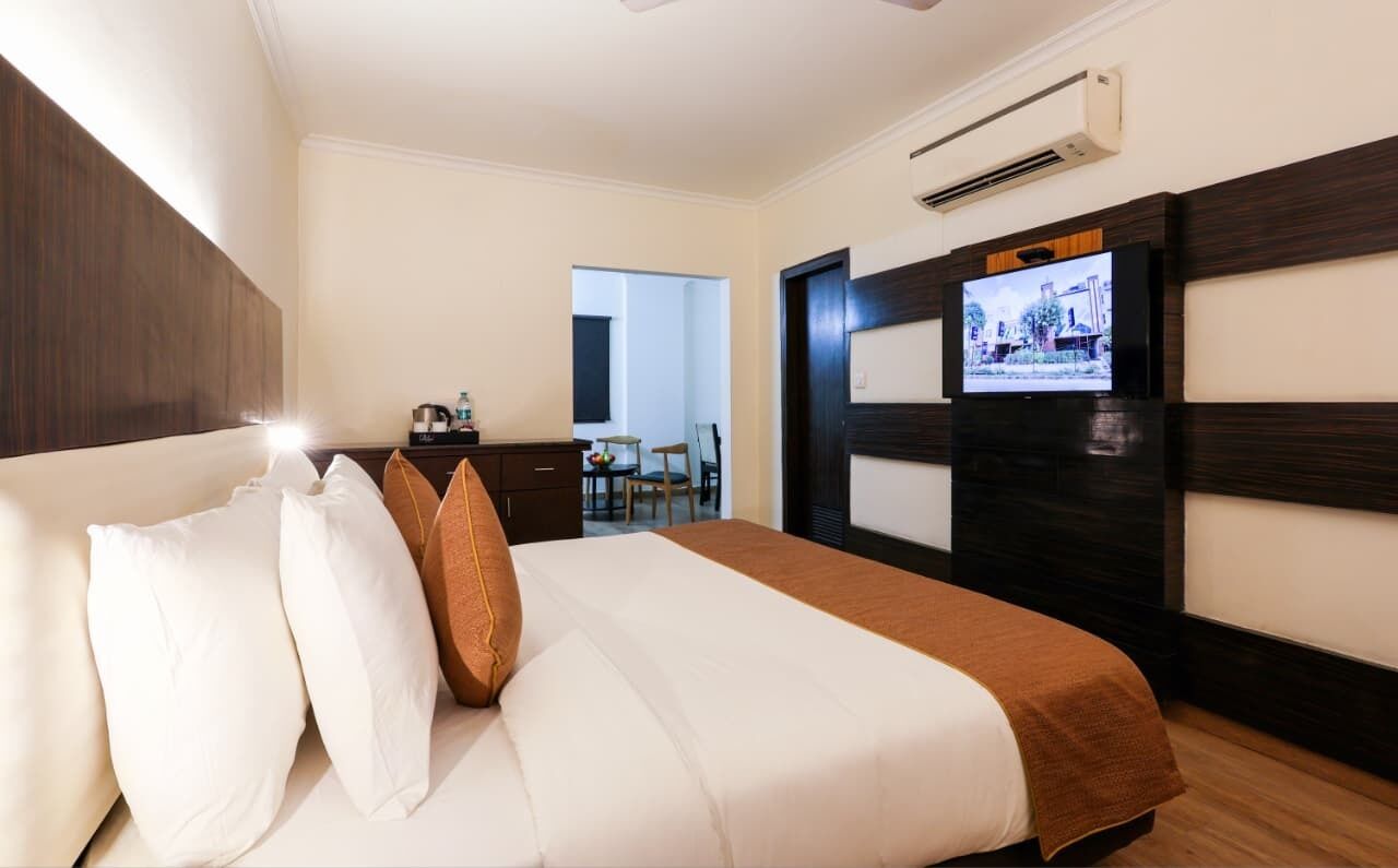 Ein Hotelzimmer mit Bett, Kissen, einem Fernseher an der Wand, einem Schreibtisch mit Stuhl und einer Klimaanlage.