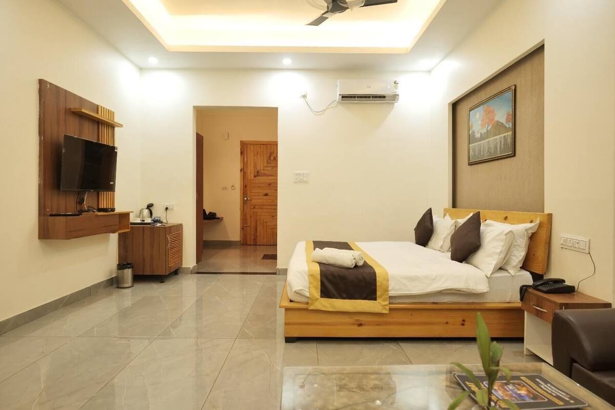 A modern hotel room with a wooden bed, a TV mounted on the wall, a desk with a trash bin, and a ceiling fan.