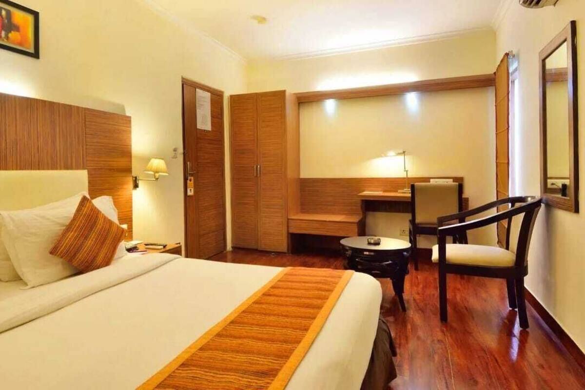A hotel room with a bed, a desk, a chair, and a small table.