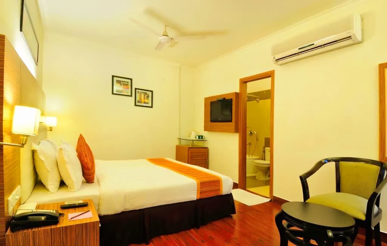 A hotel room with a bed, bedside table, chair, and a television.