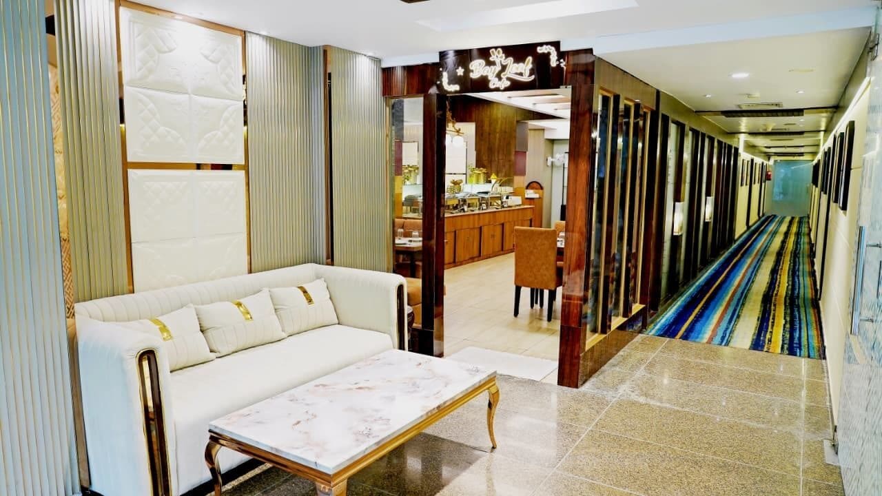 A hotel lobby with a sofa, a coffee table, a patterned rug, and a view into the dining area.