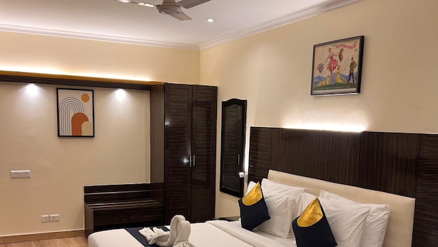 Une chambre d’hôtel avec un lit, un bureau, une chaise, un ventilateur de plafond et un tableau au mur.