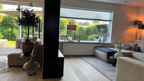 A modern living room with a large window, a black floor lamp, and a sofa. - Beautiful Country Home for 6 (Sint Maartensvlotbrug)