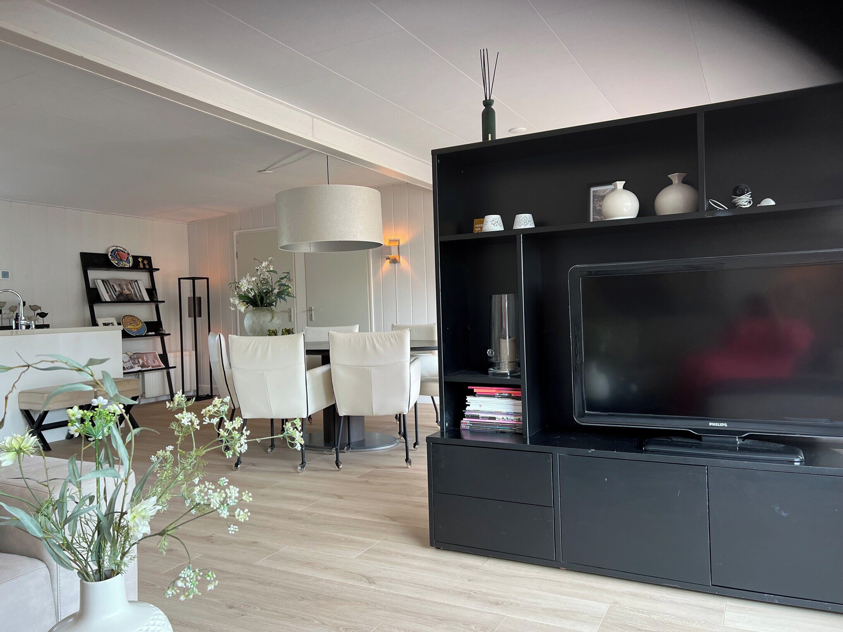 Ein modernes Wohnzimmer mit einer schwarzen Unterhaltungseinheit, einem großen Flachbildfernseher und einem Essbereich mit weißem Tisch und Stühlen.