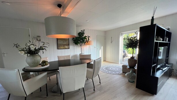 A modern dining area with a dark wooden table, white chairs, and a large pendant light. - Beautiful Country Home for 6 (Sint Maartensvlotbrug)