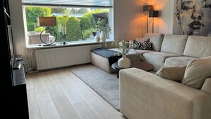 A modern living room with a sofa, a round coffee table, a radiator, a window with blinds, and a painting on the wall. - Beautiful Country Home for 6 (Sint Maartensvlotbrug)
