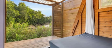 A wooden cabin with a bed, a window, and a view of a forest.