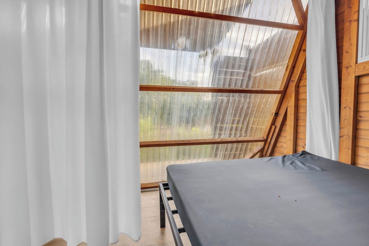 Ein Zimmer mit einem Bett, Holzwänden und einem großen Fenster mit Vorhängen.